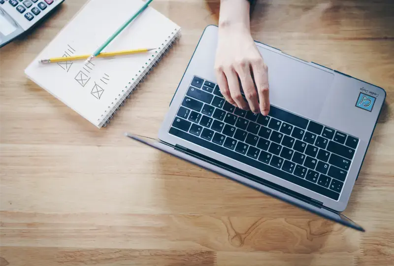 laptop with CJ Creative Design logo next to a notebook with the rough webpage blurb design sketch