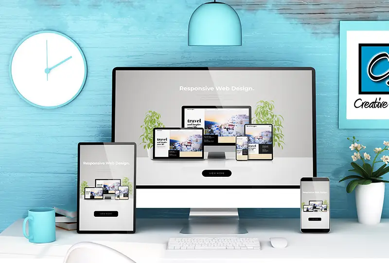 web-portfolio desk with computers showing responsive web design examples. CJ Creative Design logo is framed on the wall